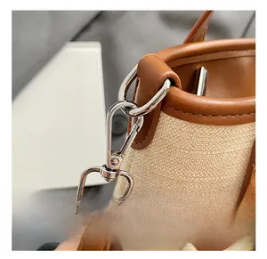 Detail of silver swivel hook with brown leather trim on beige canvas handbag