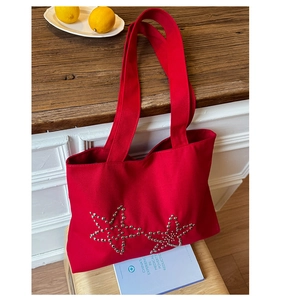 Detailed view of red canvas tote bag with silver metal rivet star patterns on a table