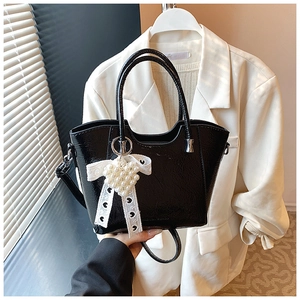 Detail of black glossy patent bucket bag featuring pearl heart and lace ribbon charm