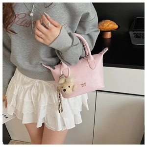 Détail du sac seau en cuir rose avec logo de la marque et breloque peluche de chien