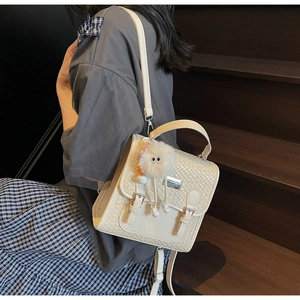 Détail du sac à dos blanc crème avec pendentif en peluche et logo en métal argenté