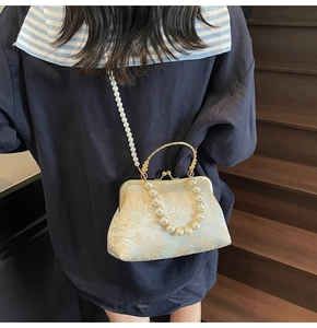 Model wearing a retro cream jacquard bag with pearl strap and gold metal handle details