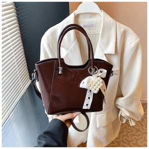 Detailed view of dark brown patent leather bucket bag with lace bow and dual handles