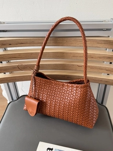 Brown hand-woven leather underarm bag with matching small pouch on a stylish seat