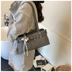 Side view of gray textured bucket bag with metal buckle and silver bow pendant charm
