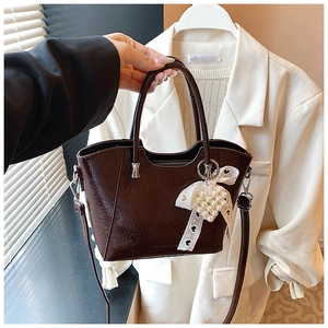 Detail of dark brown patent leather bucket bag with white lace bow and pearl charm