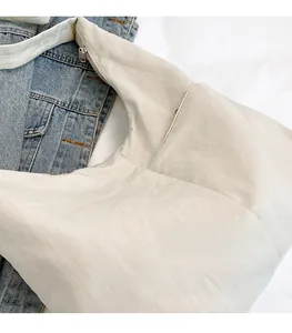 Detail of off-white hobo bag with wide strap and zipper on casual denim jacket