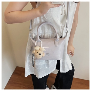 Détail d'un sac seau en cuir lavande avec pendentif ours en peluche et logo en métal