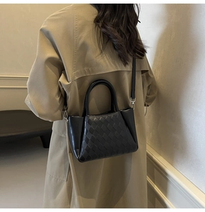 Detail shot of black woven lattice bucket bag with adjustable strap on a classic trench coat