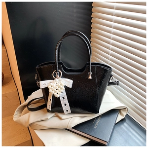 Detail of black glossy bucket bag with lace bow and pearl heart pendant decoration