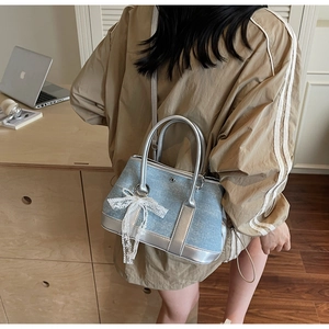 Detail der hellblauen Denim-Beuteltasche mit weißer Spitzen-Schleife und Silbergriff
