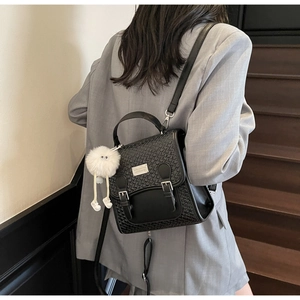Détail d'un sac à dos noir tressé avec plaque logo en métal et breloque monstre en peluche