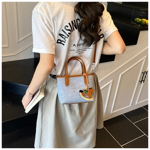 Detail of denim canvas handbag featuring brown leather trim and a wooden horse charm accessory