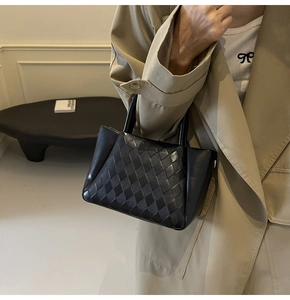 Detailed view of black quilted leather handbag with woven texture and dual handles