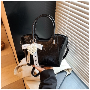 Detail of black glossy bucket bag featuring pearl heart charm and white bow decoration