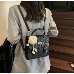 Détail d'un sac à dos noir texturé avec breloque décorative et finitions métal