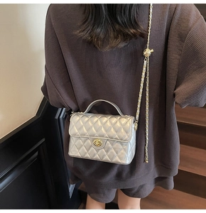 Detail of silver quilted small square bag with gold twist lock and chain strap on shoulder