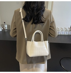 Rear view of model holding a white quilted bucket bag with a brown blazer jacket
