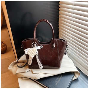Detail of dark brown glossy bucket bag with lace bow and pearl heart charm accessory