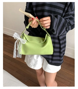 Detail of light green dumpling bag featuring white lace and pearl bow charms on textured leather