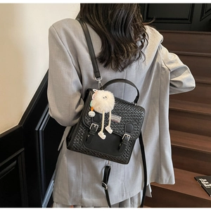 Détail d'un sac à dos tissé noir avec boucle argentée et pompon sur veste grise