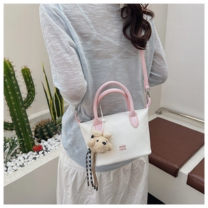Sac seau blanc chic avec poignées roses et breloque ours en peluche porté par un mannequin