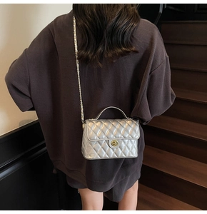 Detailed view of silver quilted crossbody bag with gold twist lock and chain strap