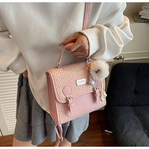 Détail du sac à dos en similicuir rose avec rabat tressé et pendentif en peluche blanche