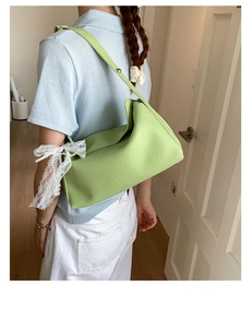Close-up of grass green shoulder bag with white lace bow and pearl beads detail