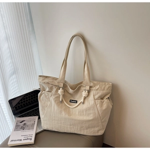 Detail of beige nylon tote bag with knot decoration and functional drawstring side pocket