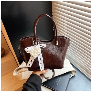 Detail of dark brown leather bucket bag with lace bow and pearl heart charm accessory
