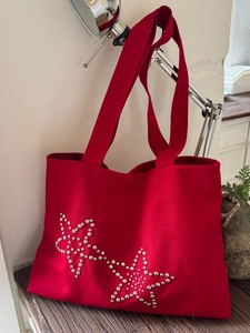 Red canvas tote bag with silver metal star studs shown in a modern home interior setting