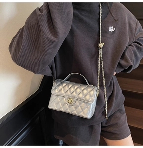 Detail of silver quilted handbag with golden twist lock and chain strap on dark background