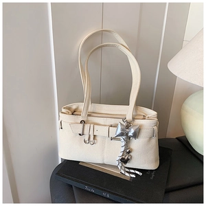 Detail of cream white bucket bag with silver butterfly and heart pendants on a book