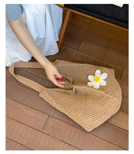 Detail einer khakifarbenen Häkeltasche mit hohlem Strickmuster und weißer Gänseblümchen