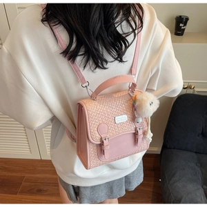 Détail du sac à dos rose en similicuir avec rabat tressé et charmant pompon blanc doux