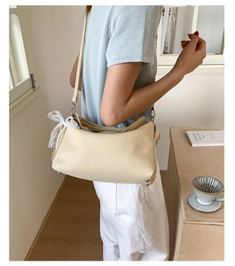 Detail of beige lychee leather crossbody bag featuring a white lace bow and slim strap