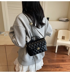 Detail of black quilted leather crossbody bag with gold chain and metal adjustment ball