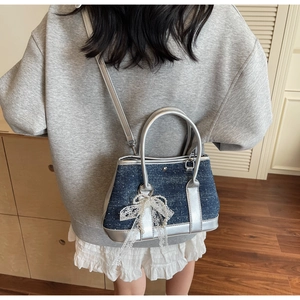 Detail of denim crossbody bag with silver mirror leather trim and pearl bow charm