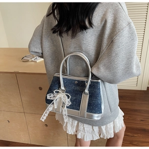 Detail der Denim-Eimertasche mit weißer Spitzenschleife und elegantem Perlenanhänger