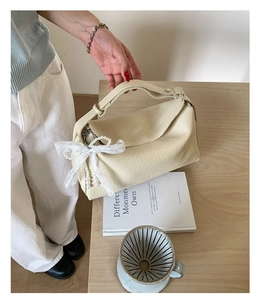 Detail of cream leather dumpling bag with lace bow and elegant pearl chain ornament
