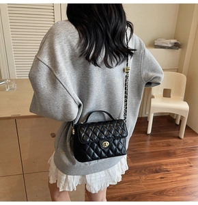 Detail of black quilted crossbody bag with golden hardware and chain strap on person