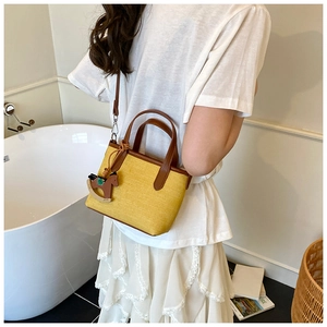 Detail of yellow woven mini bucket bag with brown leather handles and rocking horse charm