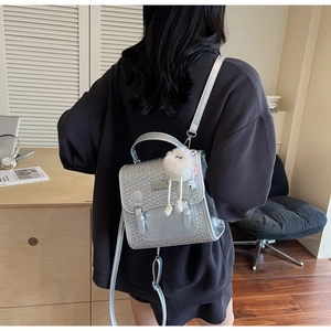 Vue détaillée du mini sac à dos argenté avec texture tissée et breloque en peluche blanche