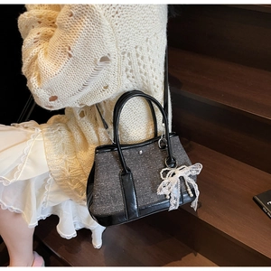 Detail der grauen Tweed-Beuteltasche mit weißer Spitzenschleife und Perlendetails