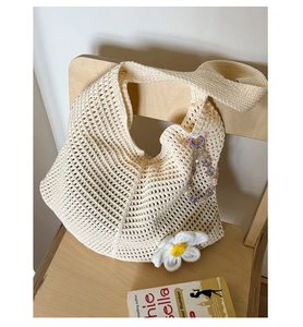 Nahaufnahme der Stricktasche mit Gänseblümchen-Details und lila Perlenanhänger auf Holz