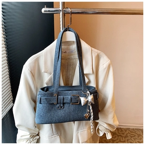 Detail of blue denim shoulder bag featuring silver bow and heart charm pendants