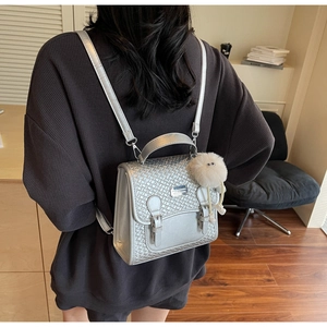 Détail du sac à dos argenté tissé avec un porte-clés en peluche blanc et boucles métal