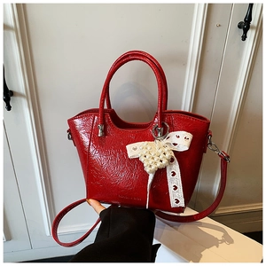 Detail of red patent leather bucket bag with lace bow and pearl heart charm