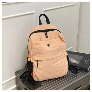 Detail of peach nylon travel backpack on luggage showing side pockets and red logo tag
